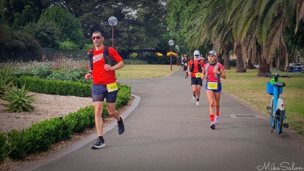 Group of Bondi‑to‑Manly Ultra runners in red shirts and hydration packs running along a paved path in Sydney