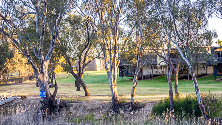 Accommodation buildings on stilts at Deep Creek Marina near Moama, framed by river gums and a blue "1660 km" Murray River distance marker.