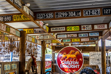 Interior of the Great Aussie Beer Shed showing vintage Australian license plates, hanging rabbit traps, and a red Carlton Draught sign surrounded by rustic timber beams.