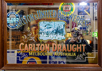 Self‑portrait reflected in a vintage Carlton Draught mirror at the Great Aussie Beer Shed, showing brewery logo with horses and cart surrounded by memorabilia.