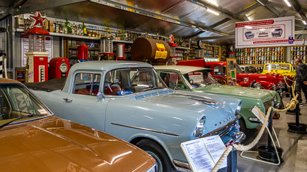 Interior of the Great Aussie Beer Shed showing vintage Holdens and classic cars surrounded by petrol pumps, Golden Fleece barrel, and shelves of oil cans and memorabilia.