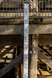 Vertical flood‑level gauge fixed to timber beams of Echuca Wharf, showing historical water heights from 1867 to 2022 with sunlight and shadow across the wooden structure.