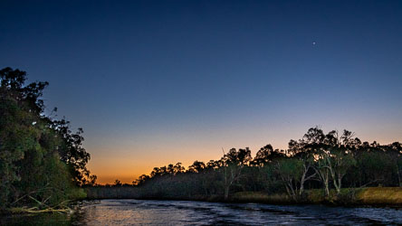 Twilight view of the Murray River with silhouetted trees and a clear sky showing Venus above the horizon, fading from orange to deep blue.