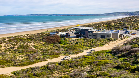 From the whale watching boardwalk, Goolwa Beach looking west showing the surfclub, parking lot, and 4WD track to the beach. [2027]