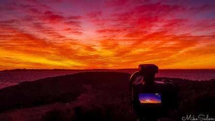 Brilliant red-orange sky at sunrise, with a camera positioned to capture it. [0029]