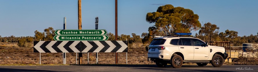 White vehicle at an intersection with directional signage and trees in background.