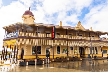 Large historic hotel with balcony and ornate roofline, wet street in foreground.