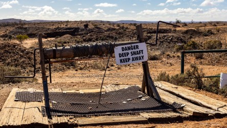 Metal grate and sign reading "Danger Deep Shaft Keep Away" in rocky outback terrain.