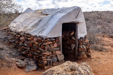 Small stone hut with cloth roof and wooden door in arid landscape.