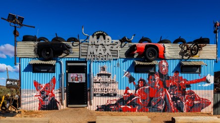 Building with "Mad Max 2 Museum" sign, painted murals, and car props attached to exterior.