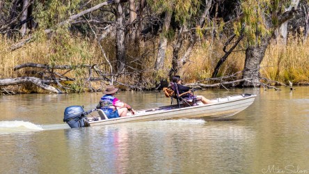  Two people in small motorboat on still river surrounded by trees.