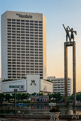 Two bronze figures atop tall pillars of the Welcome Monument with the Mandarin Hotel Jakarta behind them at sunset.