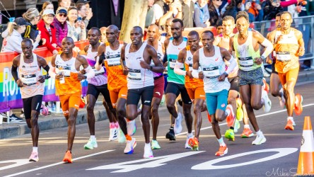 Lead pack of elite runners, including pace setters and world‑class competitors, racing through central Sydney streets at the start of the 2025 Sydney Marathon, with spectators lining the barriers.