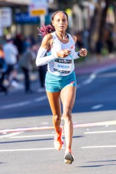 Elite female marathon runner Deressa in light blue kit running through Taylor Square toward the Sydney Opera House finish during the Sydney Marathon 2025, focused and determined under morning light.