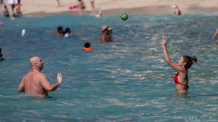 A woman reaching up to set a green ball in turquoise ocean water while a man stands nearby ready to receive it at Waikiki Beach.
