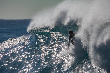 A surfer emerging through sparkling backspray and dark water as a heavy wave curls overhead at Bronte Beach.