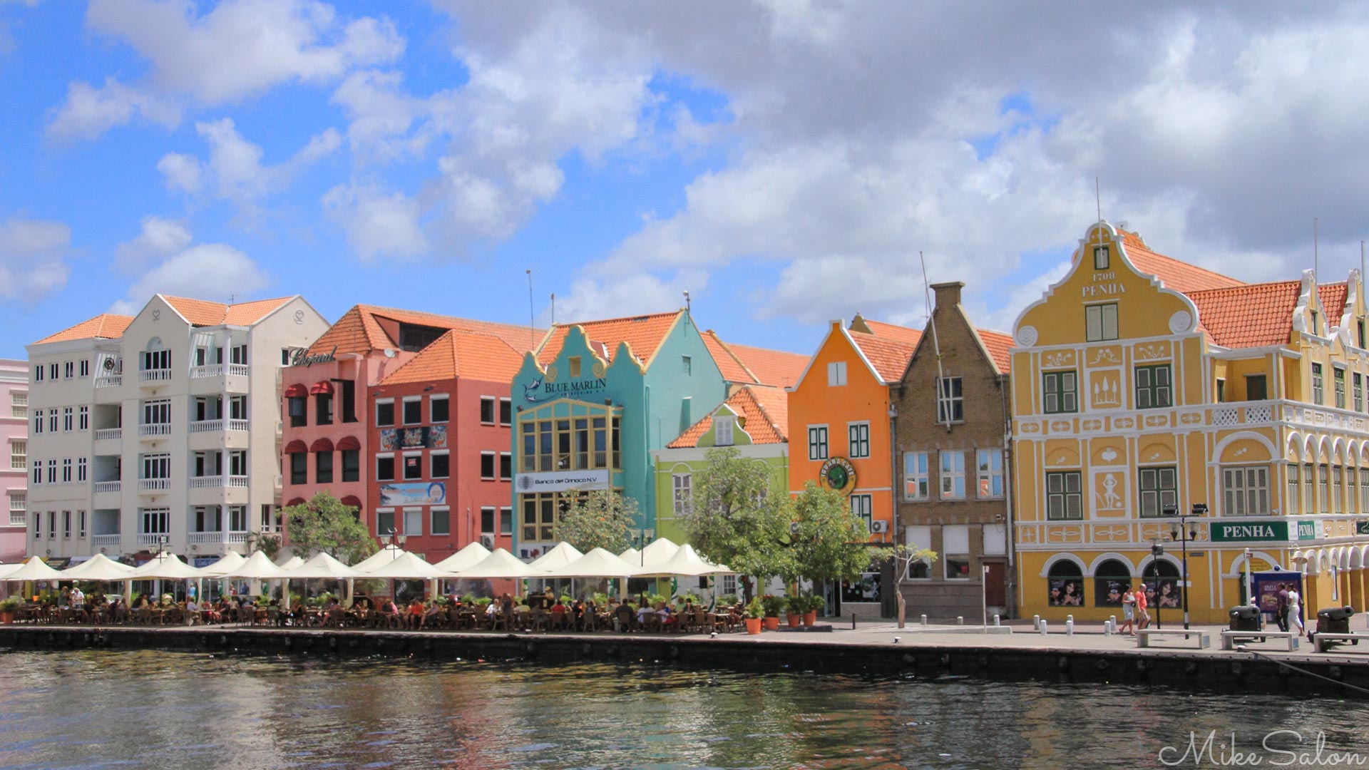 A vivid parade of Dutch‑Caribbean façades along the Punda waterfront, seen from Otrobanda. These pastel merchants A vivid parade of Dutch‑Caribbean façades along the Punda waterfront, seen from Otrobanda. These pastel merchants