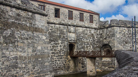 Stone fortress of Castillo de la Real Fuerza in Havana, Cuba, showing arched entrance, wooden bridge, and thick masonry walls under a partly cloudy sky.