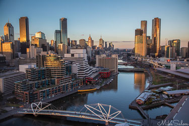 Melbourne skyline at sunset with the Yarra River and bridges reflecting golden light under a clear winter sky.