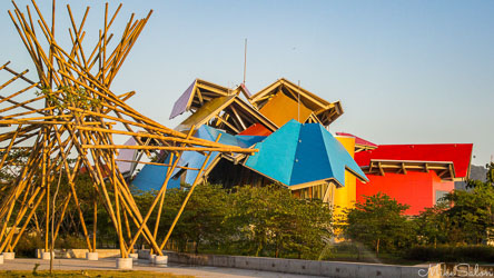 Biomuseo in Panama City with brightly coloured angular roofs and bamboo sculpture in foreground under clear blue sky.