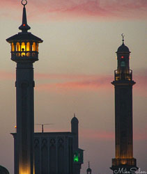 Grand Bur Dubai Mosque at sunset with illuminated minarets and domes against a pink‑orange sky.
