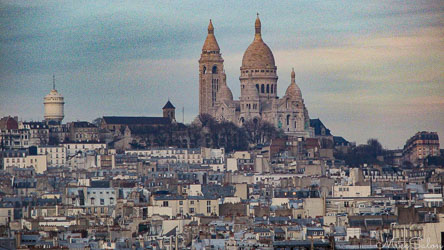 View of Sacré‑Cœur Basilica on Montmartre hill in Paris with surrounding rooftops under soft twilight sky.
