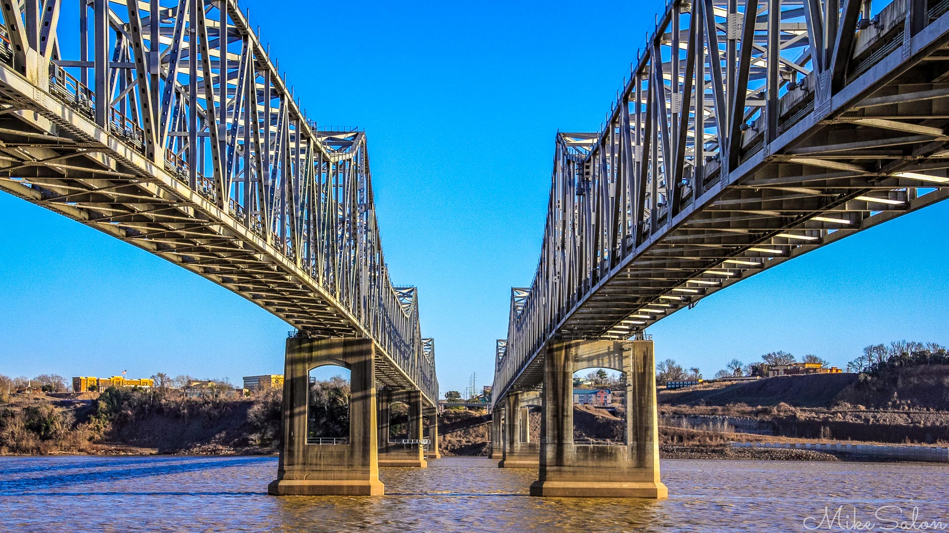 The twin steel spans of the Natchez-Vidalia Bridge link Louisiana and Mississippi across the broad brown sweep of the river. Shot from beneath on a clear winter morning, the symmetry of the trusses and the reflections in the water create a natural metaphor for connection - between places, between ideas, and between the many photographic "themes" that make up this site. Bridges like this remind us that structure and imagination can coexist beautifully: engineering precision meeting the play of light and colour.