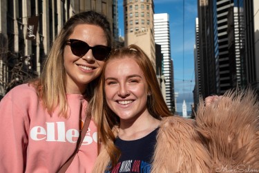 Two smiling women standing in bright sunlight among city buildings during the San Francisco Women