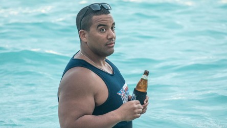 Man standing waist‑deep in turquoise water at Waikiki Beach, holding a beer bottle and enjoying the evening light.
