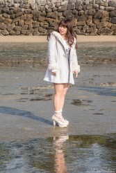 Woman in a white coat and high heels standing on the reflective mudflats at Miyajima, Japan, during low tide near the famous torii gate.