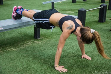 Female athlete exercising outdoors at a fitness park in Rushcutters Bay, Sydney, with feet elevated on a bench and hands on the turf.