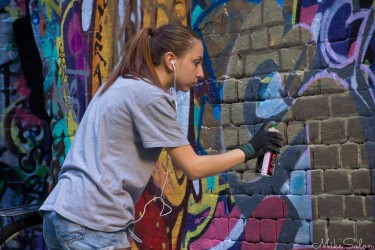 Young graffiti artist spray‑painting a colourful mural on a brick wall in Hosier Lane, Melbourne.