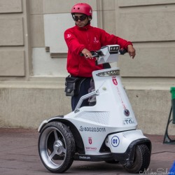 Policeman in Santiago riding a white three‑wheeled electric patrol vehicle in the Plaza de Armas, wearing a red uniform and helmet.