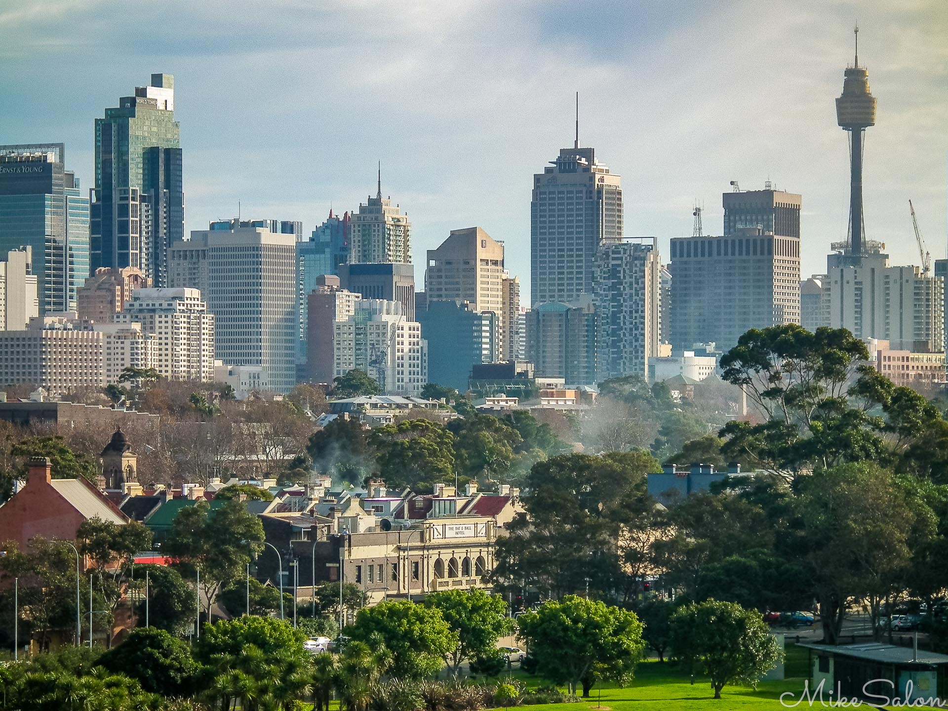 This is a view I could not resist. Captured in the soft, warm glow of morning light, this perspective offers a viewpoint on Sydney that most visitors rarely experience. In the foreground, nestled behind a dense canopy of trees, sit the historic rooflines and 19th-century Victorian terraces of Surry Hills.  Once a notorious working-class precinct marked by larrikin push gangs and poverty, the suburb has undergone a dramatic urban transformation into one of the city's most vibrant and desirable neighborhoods, its heritage architecture carefully preserved and modernized. Rising sharply directly behind it, the glass towers of the central business district and the iconic silhouette of Sydney Tower illustrate the striking juxtaposition between Sydney's historic urban grain and its towering modern identity. [4139]