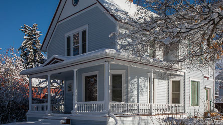 Two‑storey white wooden cottage on North Tracy Avenue in Bozeman, Montana, surrounded by snow and bare trees under clear blue sky.